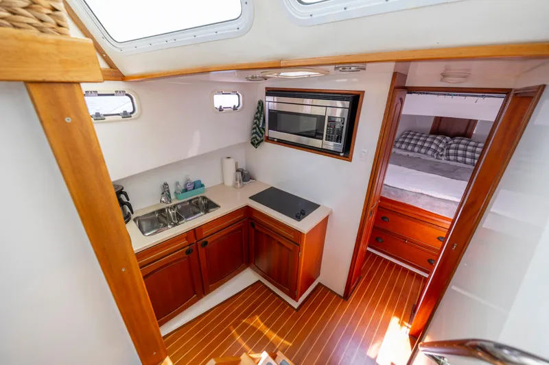 Tomahawk Yacht Photos Pics Compact boat kitchen with wooden cabinets, sink, stove, and microwave, leading to cozy bedroom.