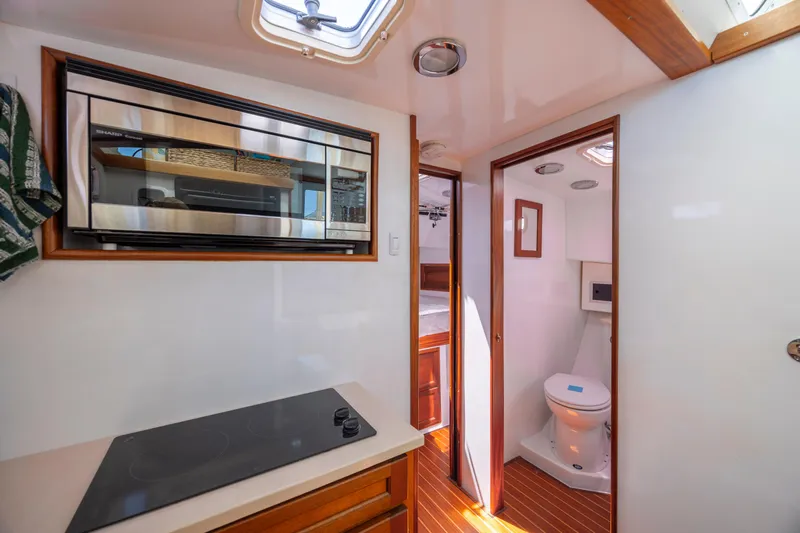 Tomahawk Yacht Photos Pics Compact boat interior with kitchenette, microwave, and bathroom, featuring wood accents and modern amenities.