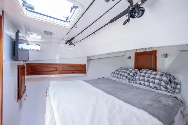 Tomahawk Yacht Photos Pics Cozy boat cabin interior with bed, plaid pillows, and wooden storage, featuring a skylight and fishing rods.