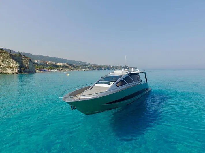 Ea Yacht Photos Pics Custom Wake 66 yacht from 2010 on clear turquoise water near a rocky coastline.