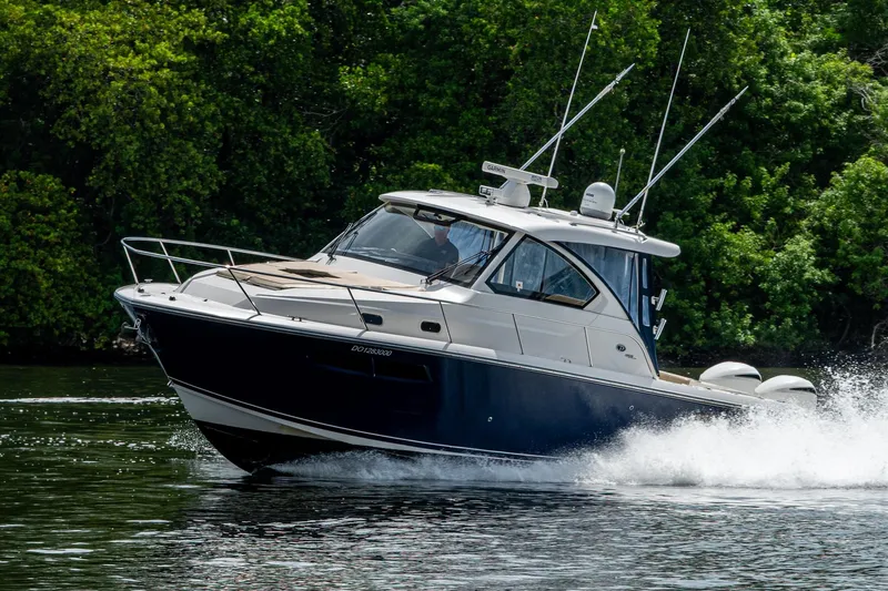  Yacht Photos Pics Pursuit boat cruising on water with lush green trees in the background.
