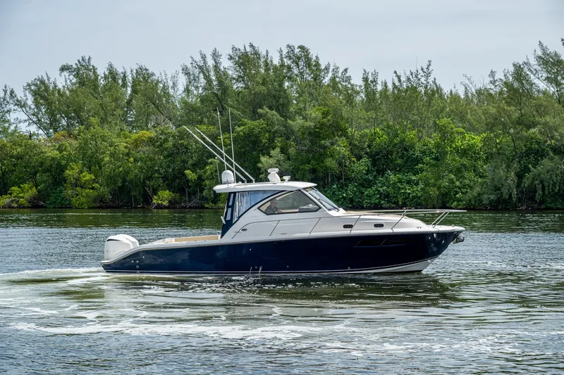  Yacht Photos Pics Pursuit boat cruising on a calm river with lush green trees in the background.