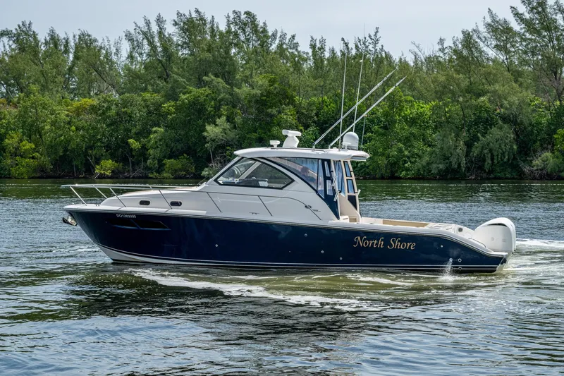  Yacht Photos Pics Pursuit boat "North Shore" cruising on a calm river with lush greenery in the background.