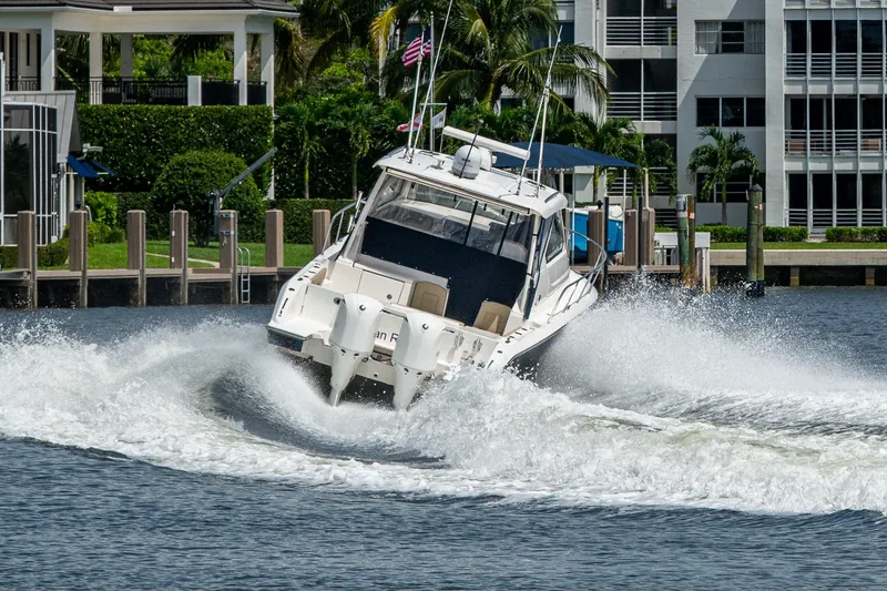  Yacht Photos Pics A Pursuit boat navigating a canal, creating a large wake near waterfront homes.