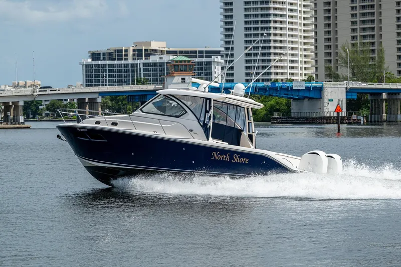  Yacht Photos Pics Pursuit boat "North Shore" cruising on water near urban bridge and buildings.