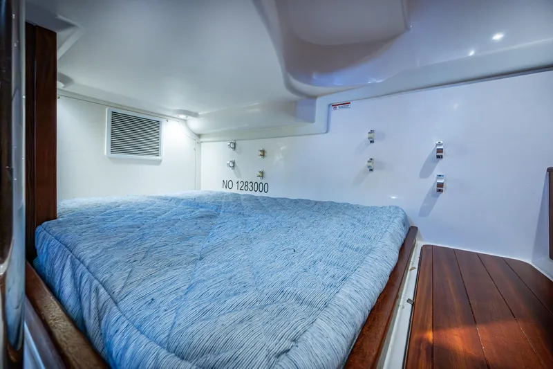  Yacht Photos Pics Cozy cabin interior with blue bedding in a Pursuit boat, featuring wood accents and white walls.