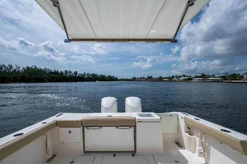  Yacht Photos Pics Pursuit boat deck with canopy, overlooking serene water and distant shoreline.