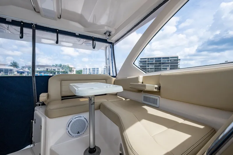  Yacht Photos Pics Interior of a Pursuit boat with beige seating and a white table, overlooking waterfront buildings.
