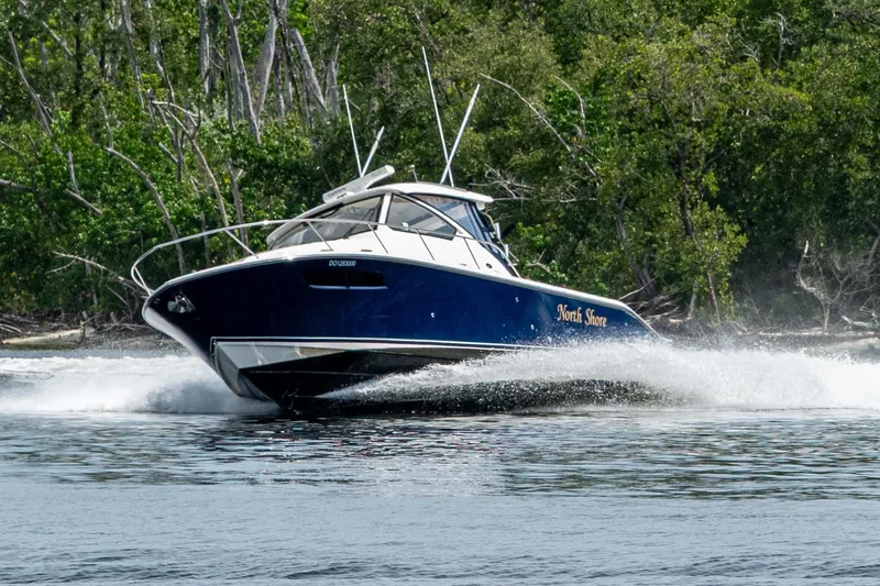  Yacht Photos Pics Pursuit boat "North Shore" cruising swiftly on water near lush green forest.