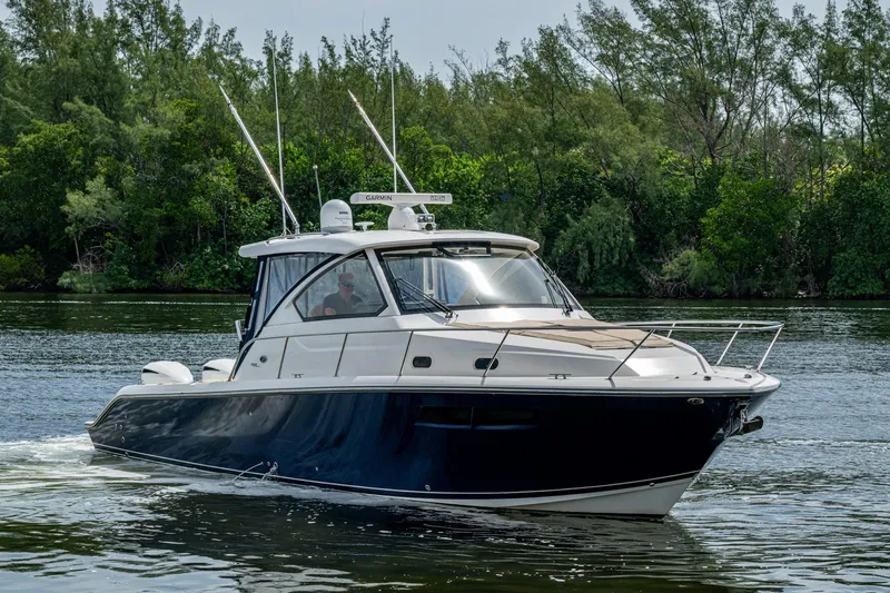  Yacht Photos Pics Pursuit boat cruising on a calm river with lush green trees in the background.
