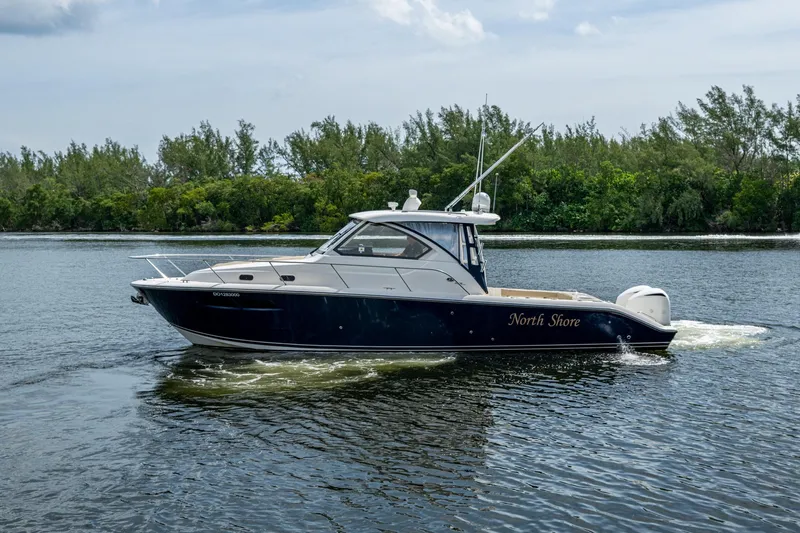  Yacht Photos Pics Pursuit boat "North Shore" cruising on a calm river with lush green trees.