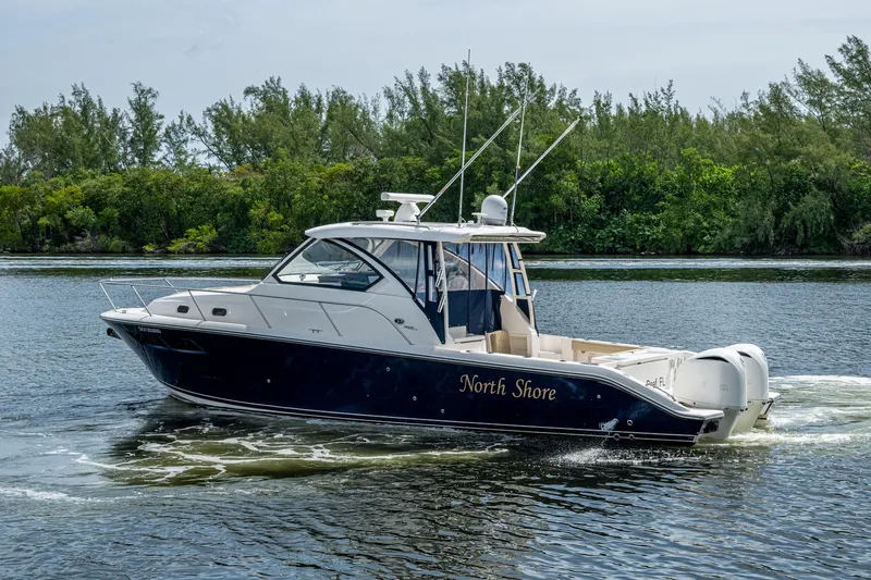  Yacht Photos Pics Pursuit boat "North Shore" cruising on a calm river with lush green trees.