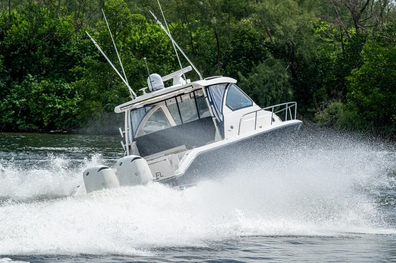  Yacht Photos Pics A Pursuit boat speeding on water, creating a large wake, surrounded by lush greenery.