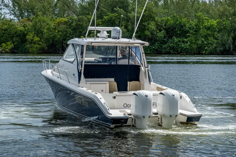  Yacht Photos Pics Pursuit boat cruising on a river with dual outboard engines, surrounded by lush greenery.