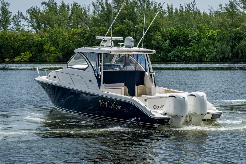  Yacht Photos Pics Pursuit boat cruising on a calm river with lush green trees in the background.