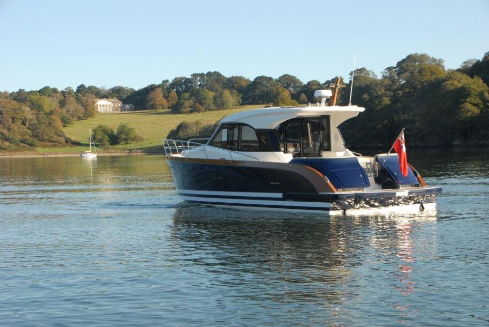 2025 Rustler 41 yacht cruising on a serene lake with lush green hills in the background.