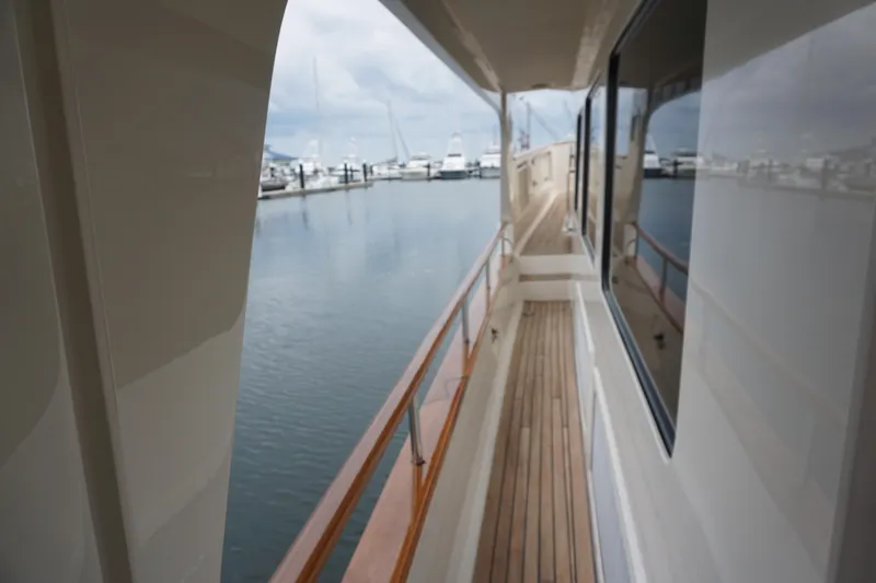 Novia II Yacht Photos Pics Side deck view of 2020 Marlow 66E yacht, featuring wooden railings and marina backdrop.