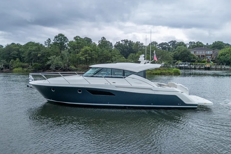  Yacht Photos Pics 2020 Tiara Yachts C44 Coupe on a serene waterway, surrounded by lush greenery.