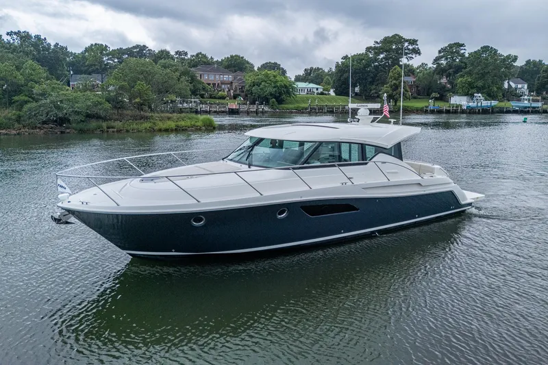  Yacht Photos Pics 2020 Tiara Yachts C44 Coupe cruising on a serene lake with lush greenery.