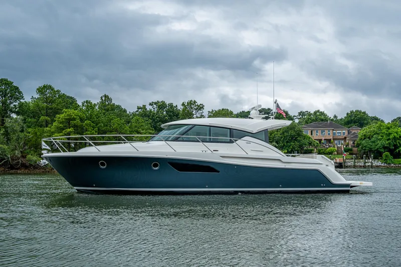  Yacht Photos Pics 2020 Tiara Yachts C44 Coupe on a serene waterway, surrounded by lush greenery.
