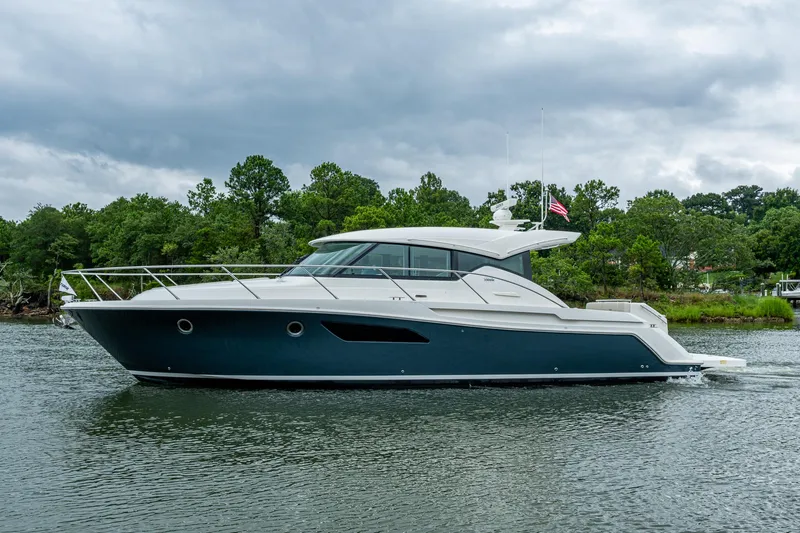  Yacht Photos Pics 2020 Tiara Yachts C44 Coupe cruising on a serene waterway with lush greenery.
