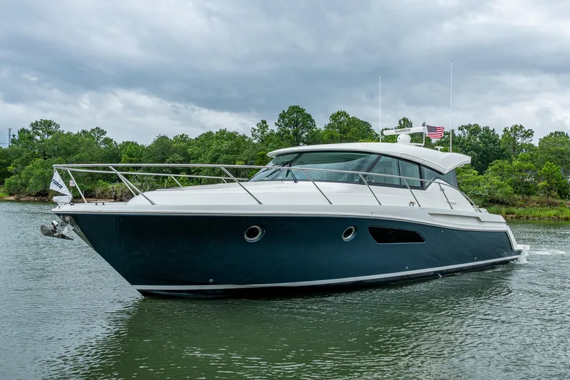  Yacht Photos Pics 2020 Tiara Yachts C44 Coupe cruising on a serene waterway with lush greenery.