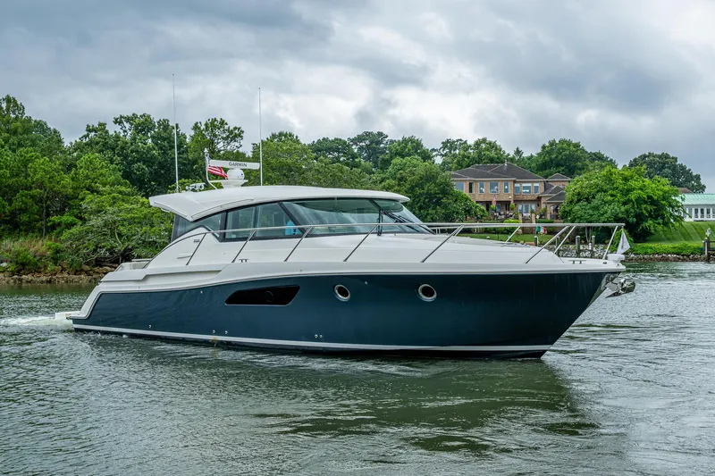  Yacht Photos Pics 2020 Tiara Yachts C44 Coupe cruising on a scenic waterway with lush greenery.