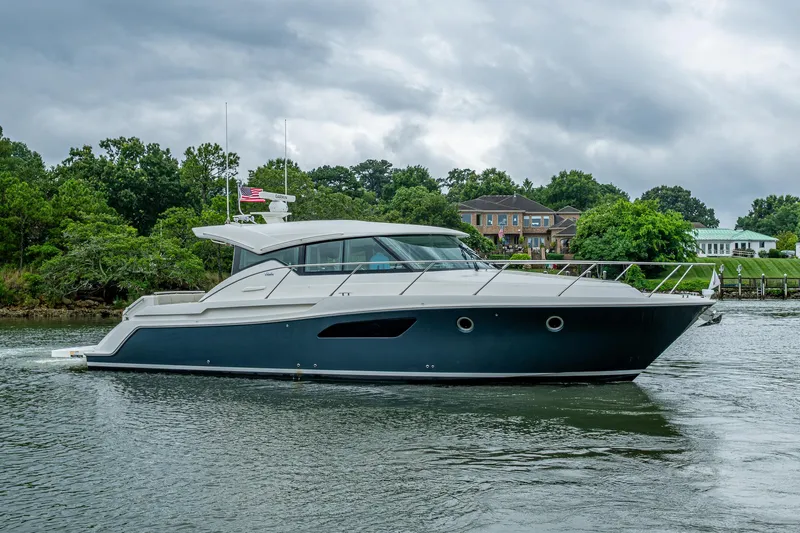  Yacht Photos Pics 2020 Tiara Yachts C44 Coupe cruising on a scenic waterway with lush greenery.