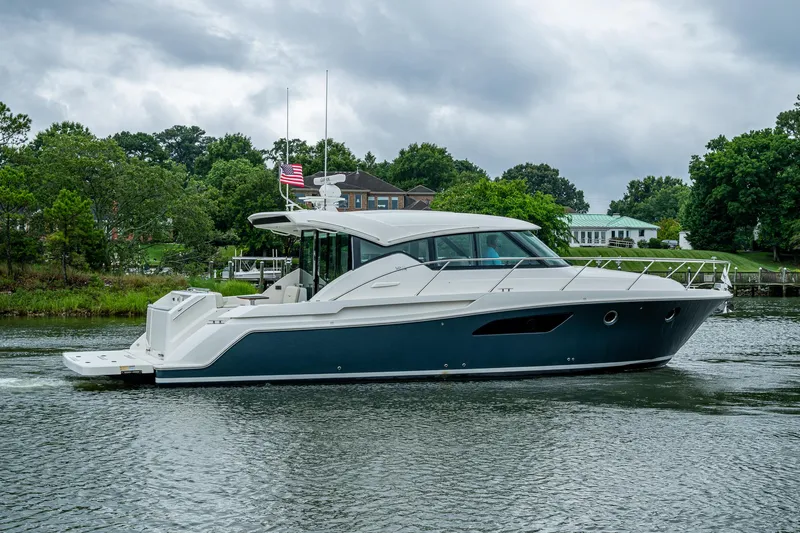 Yacht Photos Pics 2020 Tiara Yachts C44 Coupe cruising on a scenic waterway with lush greenery.