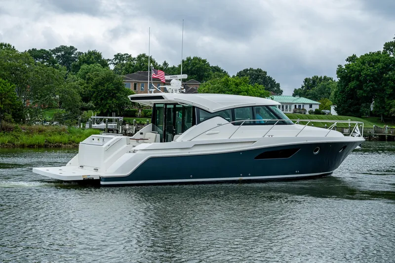  Yacht Photos Pics 2020 Tiara Yachts C44 Coupe cruising on a serene waterway, surrounded by lush greenery.