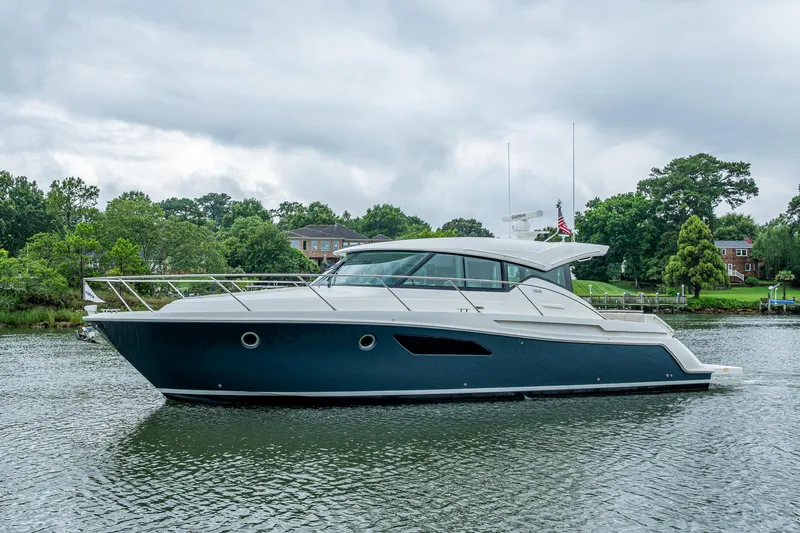 Yacht Photos Pics 2020 Tiara Yachts C44 Coupe on a serene waterway, surrounded by lush greenery.