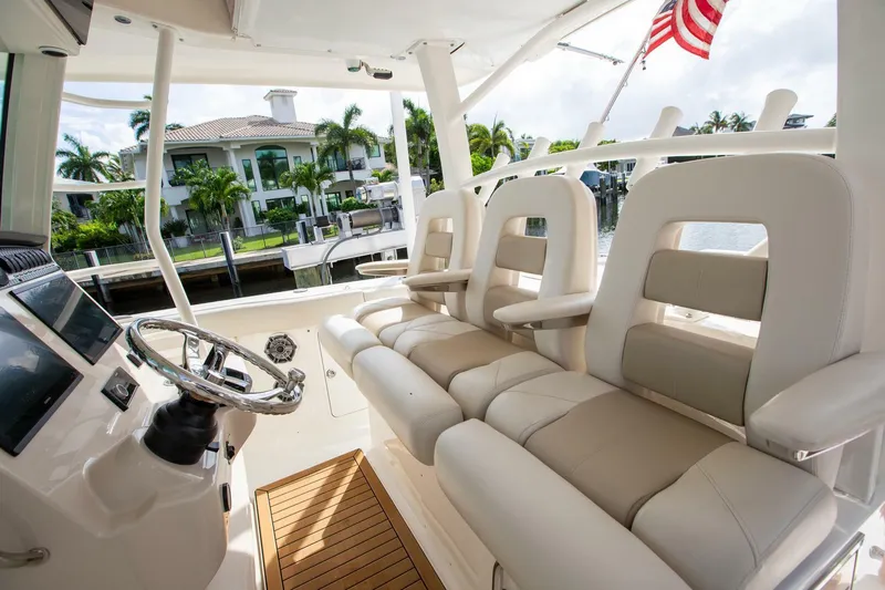 Double Nickel Yacht Photos Pics 2023 Boston Whaler 380 Outrage interior with luxurious seating and steering wheel, docked by waterfront homes.