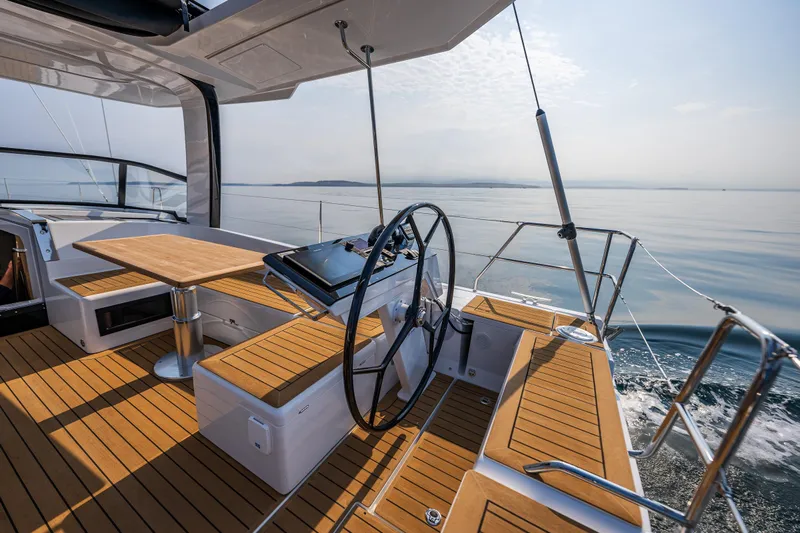 San-197 Yacht Photos Pics 2025 Hanse 460 yacht cockpit with wooden deck, steering wheel, and seating area on calm sea.