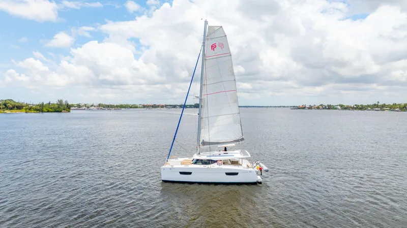 Sabai Sabai Yacht Photos Pics 2018 Fountaine Pajot Lucia 40 catamaran sailing on a calm, scenic waterway.