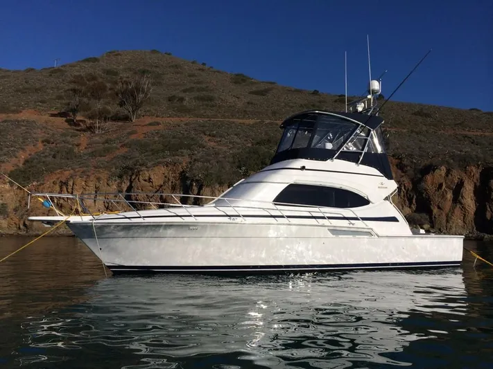 Mai Time Yacht Photos Pics 2001 Bertram 390 Convertible yacht anchored near rocky shoreline under clear blue sky.