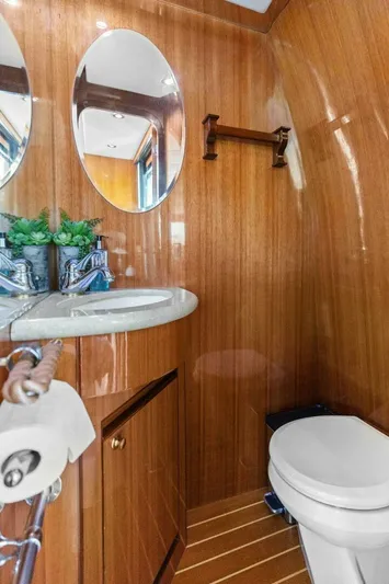 Sunshine And Happiness Yacht Photos Pics Wood-paneled bathroom with oval mirrors, sink, and toilet; modern and compact design.