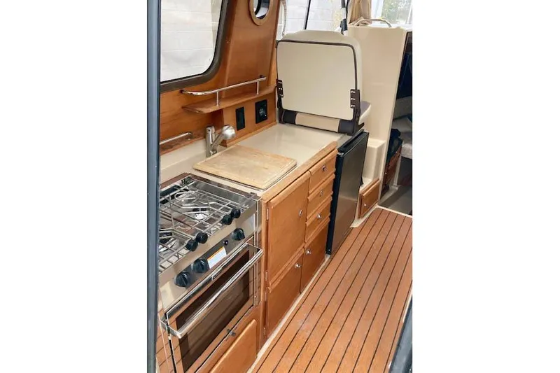  Yacht Photos Pics 2018 Ranger Tugs R-27 interior kitchen with stove, wooden cabinetry, and compact design.