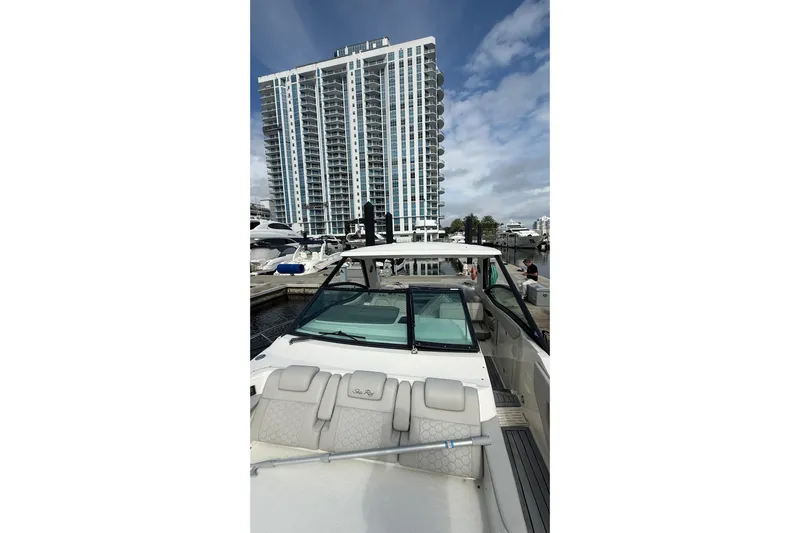 Mercy Yacht Photos Pics 2021 Sea Ray Sundancer 320 yacht docked near a tall building under a cloudy sky.