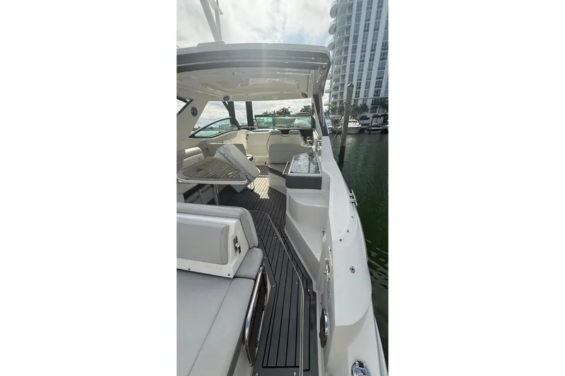 Mercy Yacht Photos Pics 2021 Sea Ray Sundancer 320 yacht interior with seating and table, docked near a high-rise building.