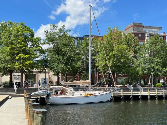 Moonsplash Yacht Photos Pics 1987 Island Packet 38 sailboat docked by a waterfront park with trees and buildings.