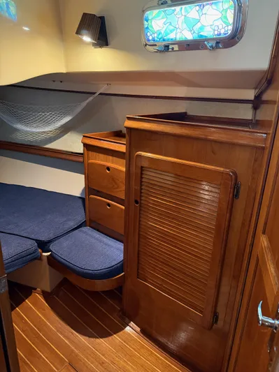 Moonsplash Yacht Photos Pics 1987 Island Packet 38 cabin interior with wooden cabinetry, blue cushions, and decorative window.