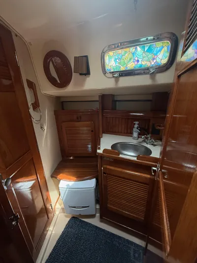 Moonsplash Yacht Photos Pics Interior of 1987 Island Packet 38 sailboat bathroom with wooden cabinetry and stained glass window.