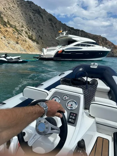 Bliss Yacht Photos Pics Person steering boat towards anchored 2015 Princess V72 yacht near rocky coastline.