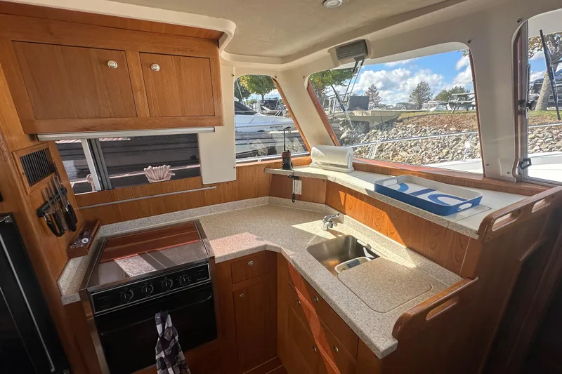 Lucky Dog Yacht Photos Pics 2002 Mainship 390 Trawler kitchen with wood cabinetry, stove, and sink, featuring large windows.
