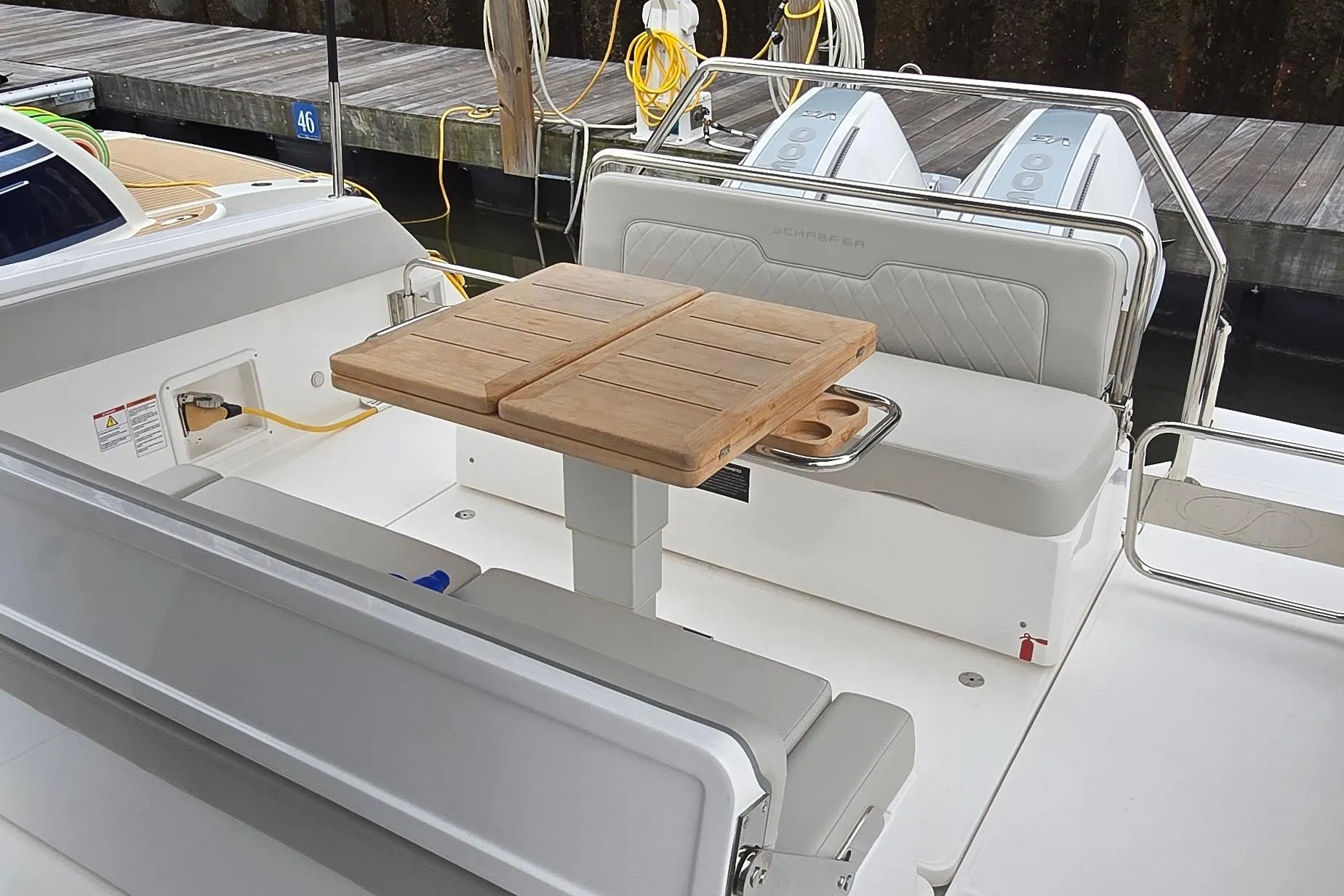 2025 Schaefer V33 boat interior with wooden table, cushioned seating, and dual outboard engines.