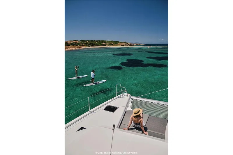  Yacht Photos Pics 2020 Dufour Catamarans 48 sailing in clear turquoise waters with paddleboarders nearby.