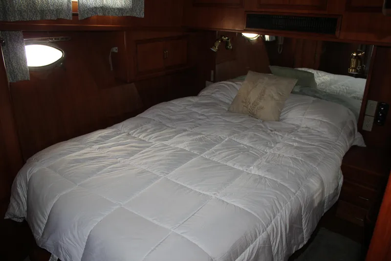 Ocean Eyes Yacht Photos Pics Cozy bedroom in a 1994 Mikelson 64 yacht with wooden interior and white bedding.