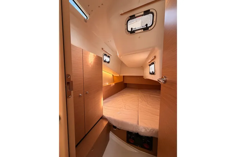 C'est Chic Yacht Photos Pics Cozy cabin interior of 2025 Jeanneau Sun Odyssey 350 sailboat, featuring wood finishes and portholes.