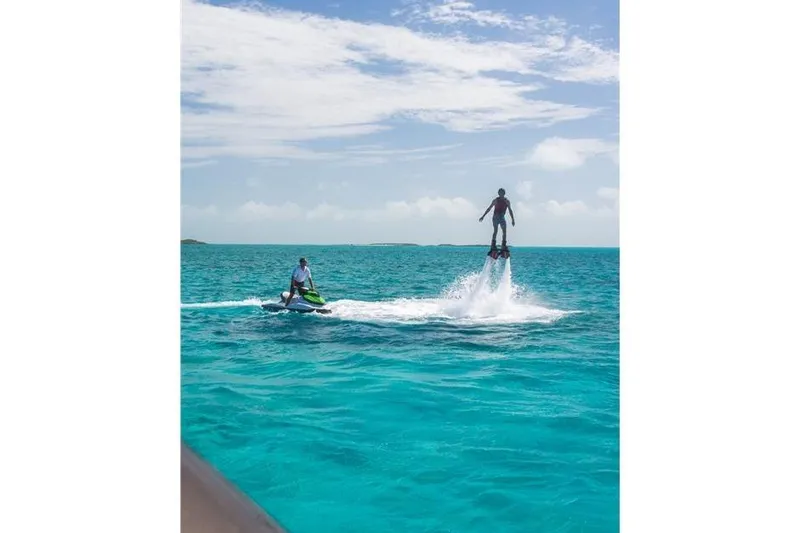 Unbridled Yacht Photos Pics Person flyboarding over turquoise ocean, accompanied by a jet ski.
