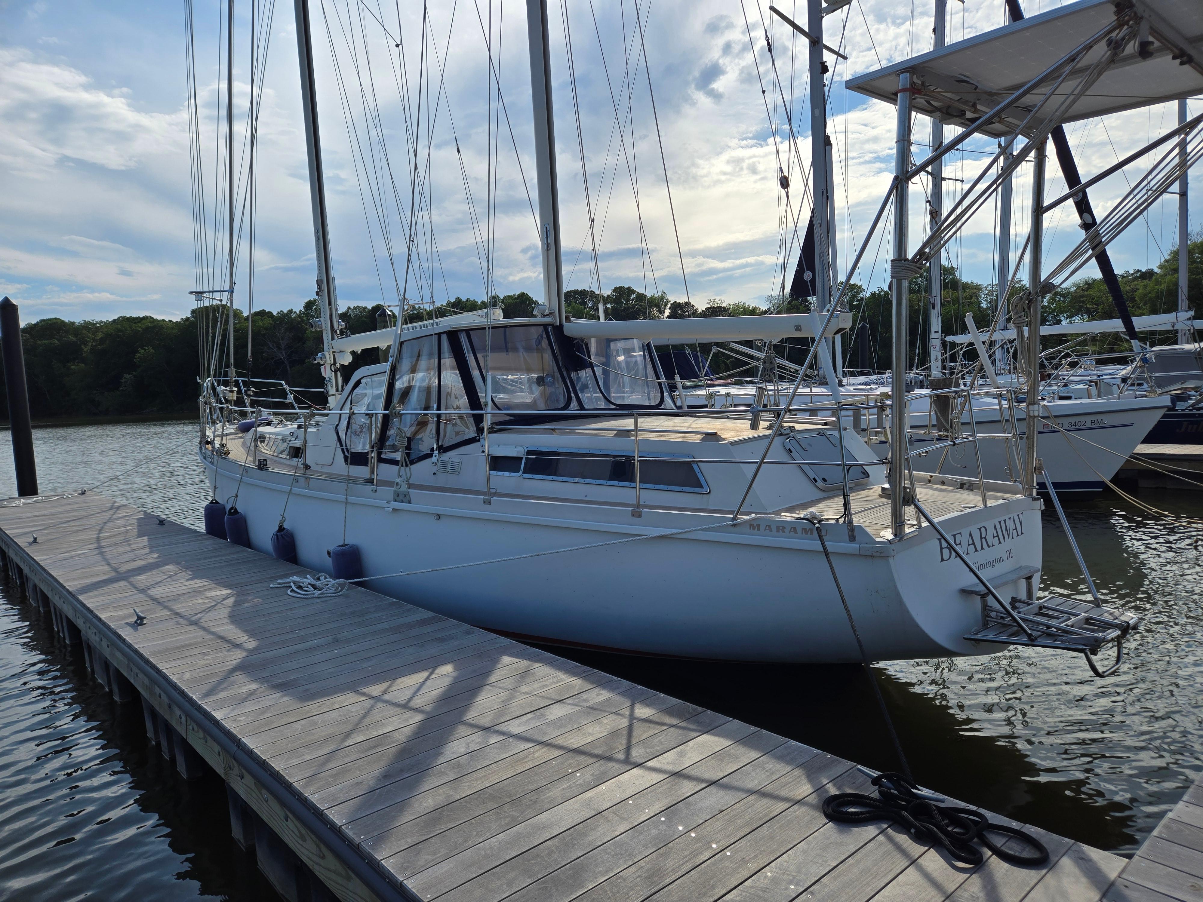 1985 Amel Maramu sailboat docked at a marina, under a partly cloudy sky.